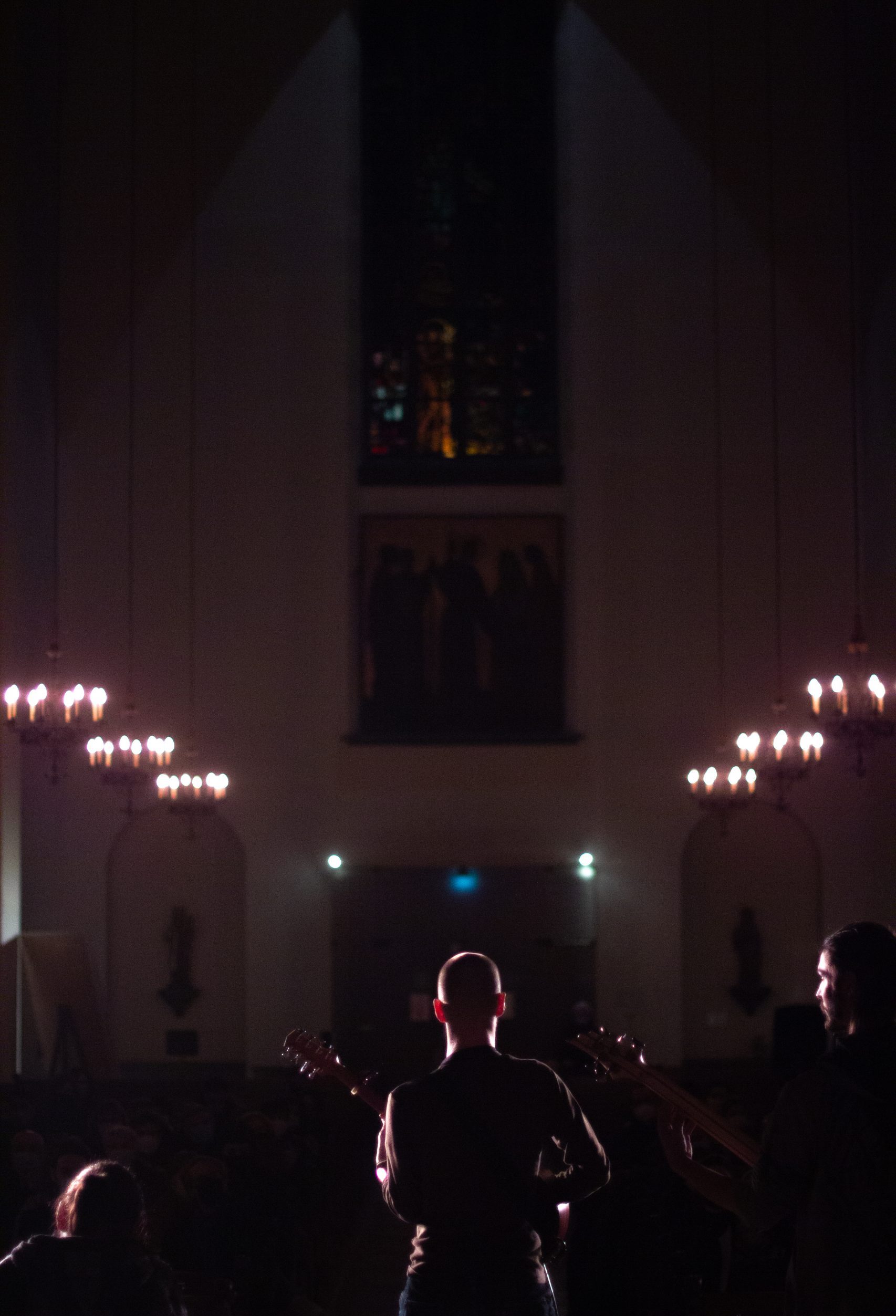 musicien jouant du bouzouki dans une église avec des lumières en fond, l'ombre se détache des ténèbres